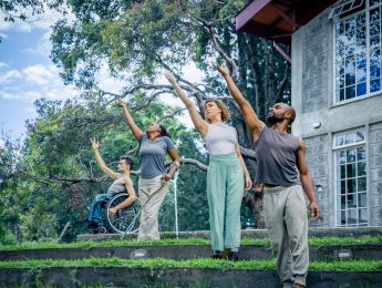 4 Performers stand in a line, all reaching their arm up. They are in a tropical garden, each on a garden step.